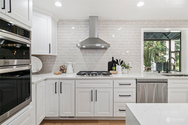 kitchen featuring sink, white cabinets, stainless steel appliances, light stone countertops, and wall chimney range hood