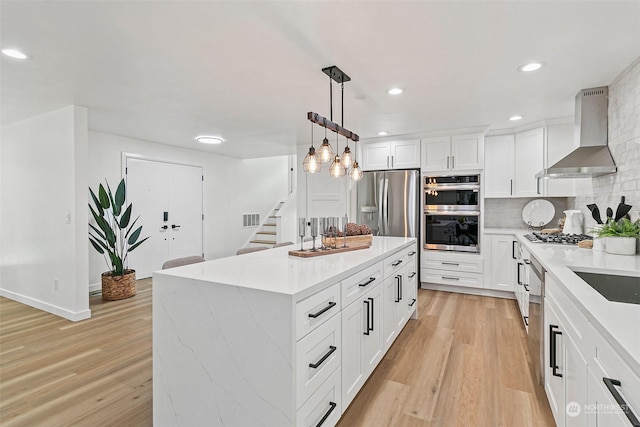 kitchen with appliances with stainless steel finishes, pendant lighting, white cabinetry, a center island, and wall chimney range hood