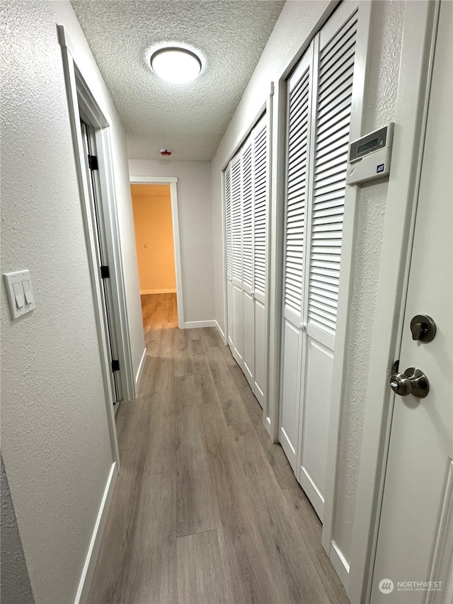 corridor with light hardwood / wood-style flooring and a textured ceiling