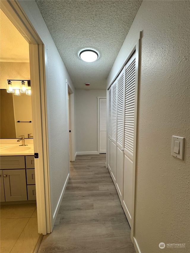 corridor with sink, light hardwood / wood-style flooring, and a textured ceiling