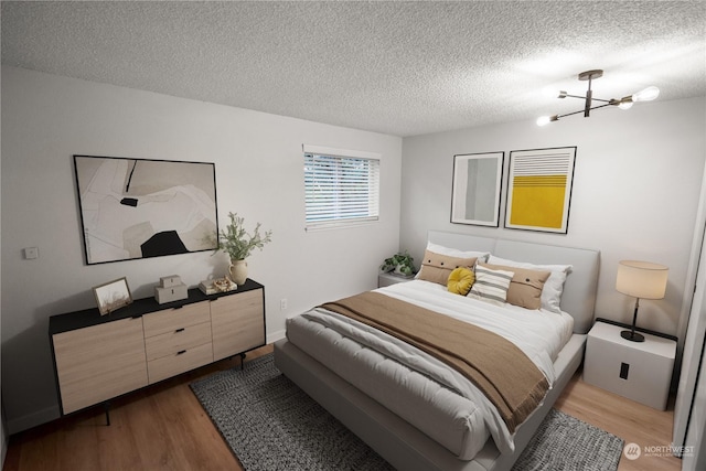 bedroom with hardwood / wood-style floors, a notable chandelier, and a textured ceiling