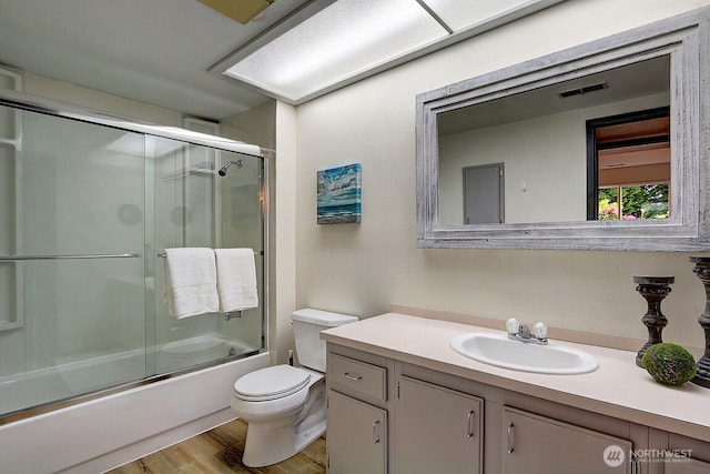 full bath with visible vents, bath / shower combo with glass door, toilet, wood finished floors, and vanity