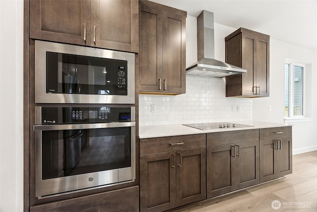 kitchen with built in microwave, tasteful backsplash, stainless steel oven, black electric cooktop, and wall chimney range hood