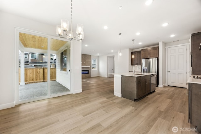 kitchen featuring sink, decorative light fixtures, stainless steel fridge, light hardwood / wood-style floors, and a kitchen island with sink