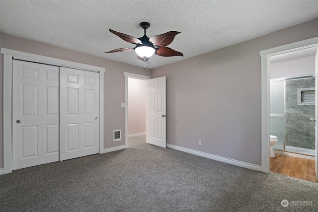 unfurnished bedroom featuring ensuite bath, dark carpet, a closet, and a textured ceiling