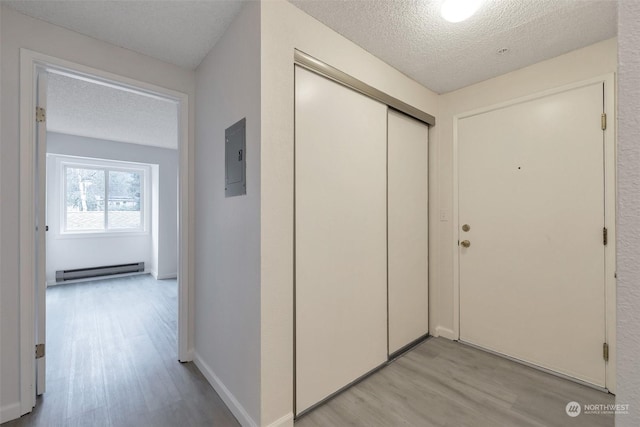 hallway featuring baseboard heating, light hardwood / wood-style floors, and a textured ceiling