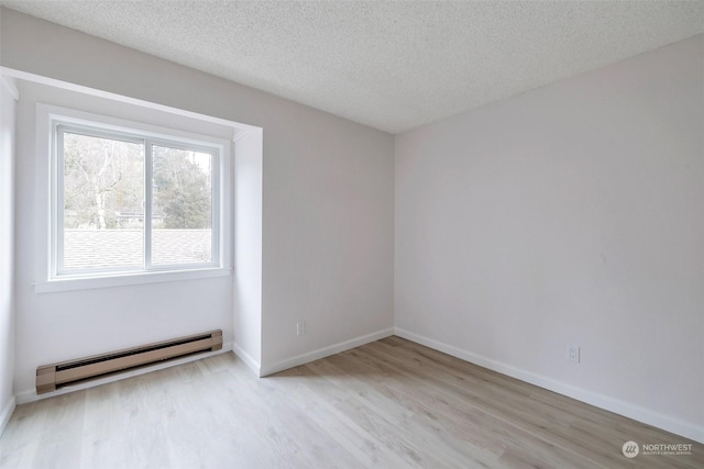 empty room featuring light hardwood / wood-style flooring, a baseboard radiator, and a textured ceiling