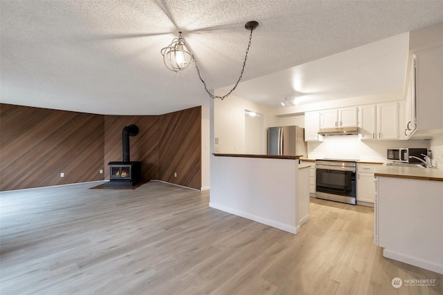 kitchen with sink, wood walls, white cabinetry, appliances with stainless steel finishes, and pendant lighting