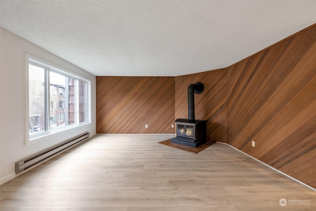 unfurnished living room featuring wooden walls, a textured ceiling, a wood stove, and a baseboard heating unit