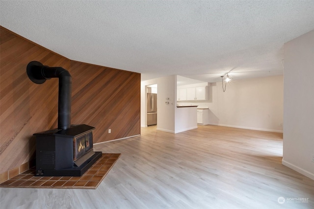 unfurnished living room with a wood stove, a textured ceiling, light wood-type flooring, and wood walls