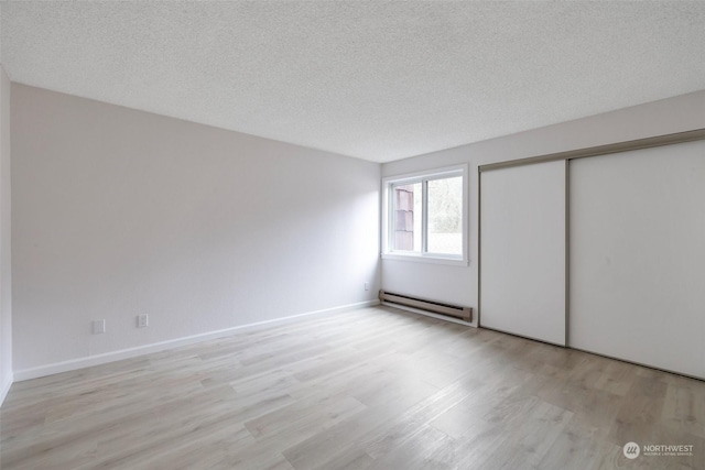 unfurnished bedroom with a closet, a textured ceiling, light hardwood / wood-style flooring, and a baseboard heating unit