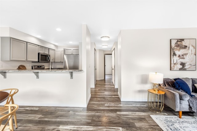 kitchen with a kitchen bar, dark hardwood / wood-style floors, gray cabinets, kitchen peninsula, and stainless steel appliances