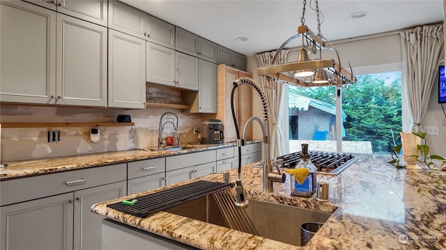 kitchen featuring gray cabinets, decorative light fixtures, sink, decorative backsplash, and light stone countertops