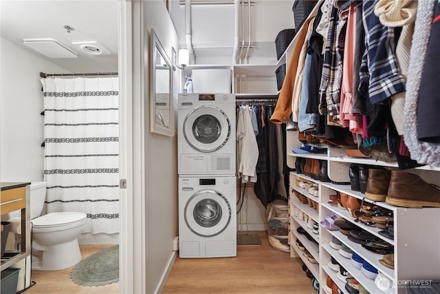 laundry room featuring stacked washer and clothes dryer and light hardwood / wood-style flooring