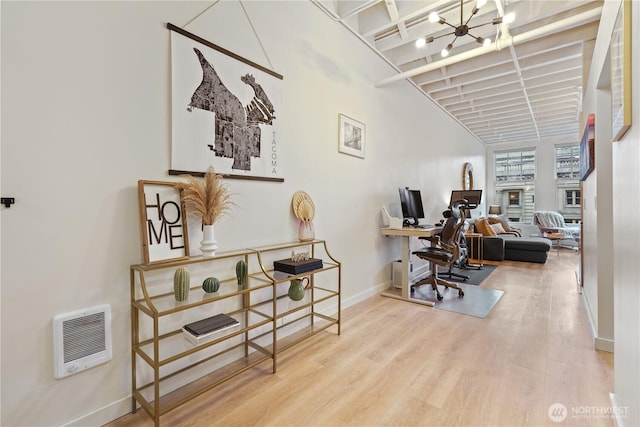 home office with a towering ceiling, heating unit, a notable chandelier, and light hardwood / wood-style floors