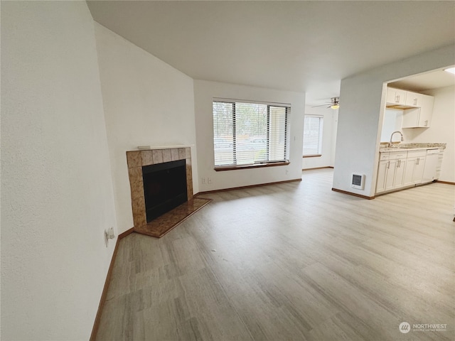 unfurnished living room featuring ceiling fan, sink, a fireplace, and light wood-type flooring