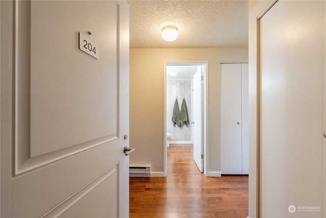 hallway with a baseboard radiator, a textured ceiling, baseboards, and wood finished floors