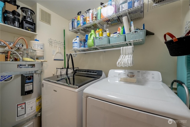 clothes washing area with washing machine and dryer, strapped water heater, visible vents, and laundry area