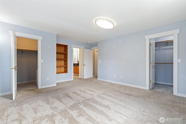 unfurnished bedroom featuring ensuite bathroom, light carpet, baseboards, a spacious closet, and a closet