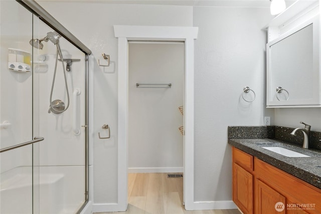 bathroom with wood finished floors, visible vents, vanity, baseboards, and a stall shower