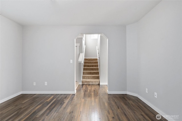 empty room featuring arched walkways, stairway, wood-type flooring, and baseboards