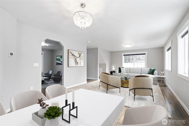 dining area featuring arched walkways, a notable chandelier, baseboards, and wood finished floors