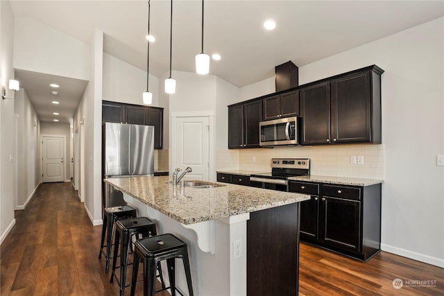 kitchen featuring appliances with stainless steel finishes, sink, hanging light fixtures, a kitchen island with sink, and light stone counters