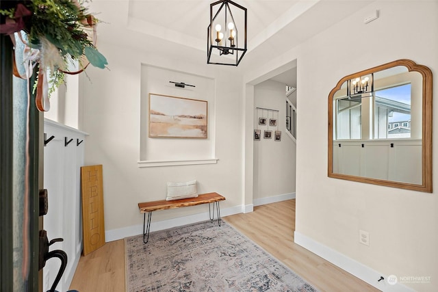 mudroom featuring a notable chandelier, a tray ceiling, and light wood-type flooring