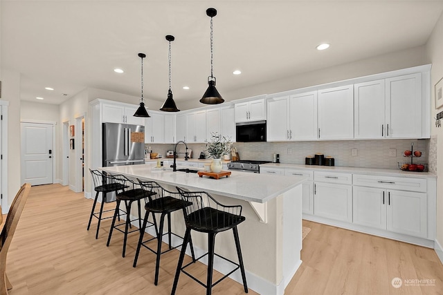 kitchen featuring a breakfast bar, pendant lighting, an island with sink, white cabinetry, and stainless steel appliances