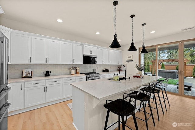 kitchen with sink, white cabinetry, decorative light fixtures, a center island with sink, and high end stainless steel range oven