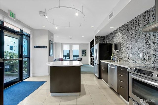 kitchen featuring decorative backsplash, a kitchen island, light tile patterned flooring, and appliances with stainless steel finishes