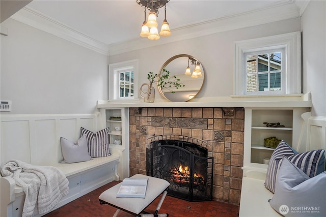 living room featuring built in shelves, a tile fireplace, a decorative wall, a wainscoted wall, and crown molding