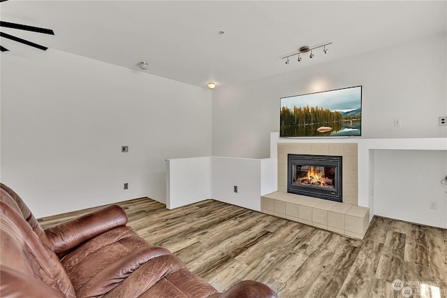 living room with a tiled fireplace, rail lighting, and light hardwood / wood-style flooring