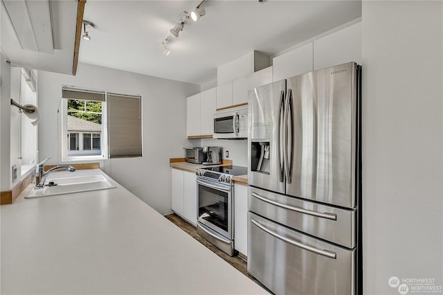 kitchen featuring white cabinetry, sink, rail lighting, and appliances with stainless steel finishes