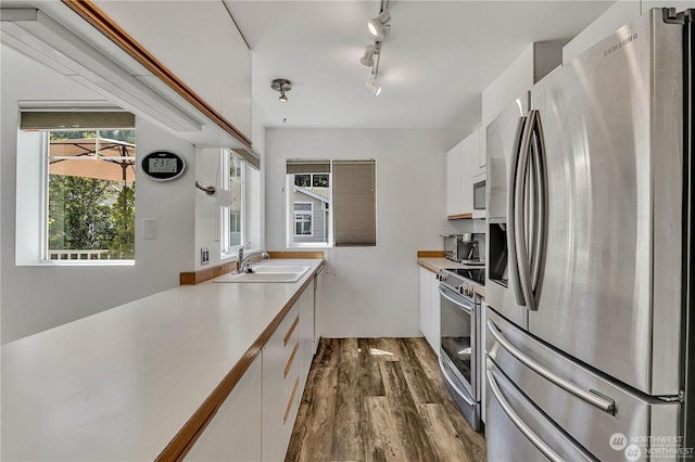 kitchen featuring sink, dark wood-type flooring, appliances with stainless steel finishes, track lighting, and white cabinets