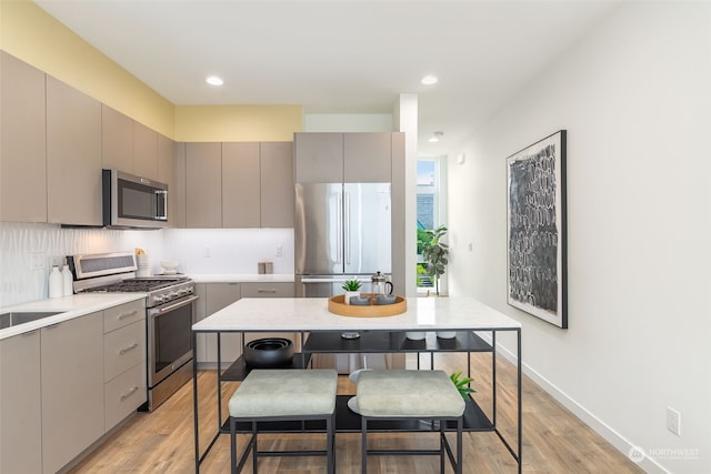 kitchen with gray cabinets, appliances with stainless steel finishes, tasteful backsplash, a center island, and light hardwood / wood-style floors