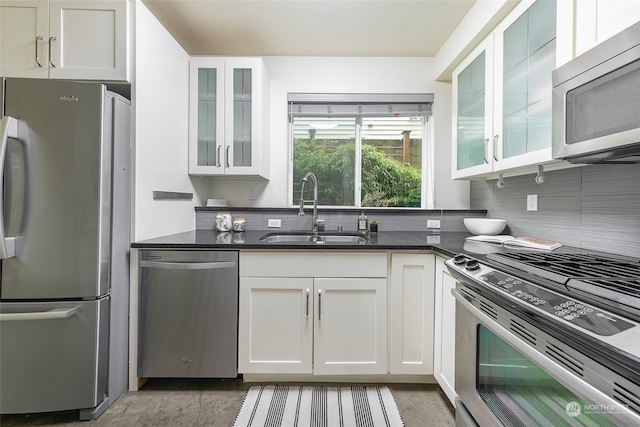 kitchen with sink, white cabinetry, dark stone counters, stainless steel appliances, and decorative backsplash