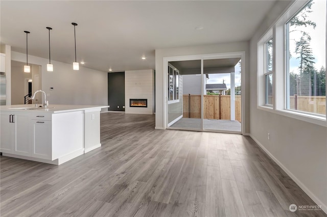 kitchen with sink, a large fireplace, an island with sink, pendant lighting, and white cabinets