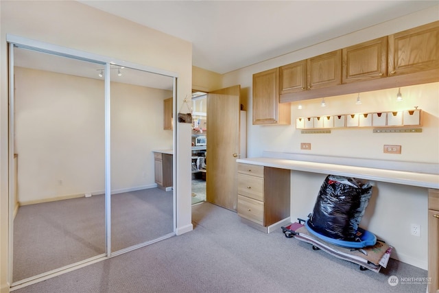 interior space featuring light brown cabinetry, built in desk, and light colored carpet