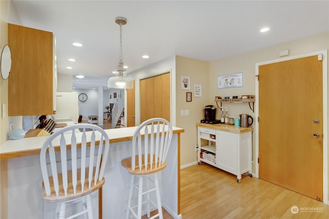 kitchen with decorative light fixtures, a breakfast bar area, white cabinets, and light wood-type flooring