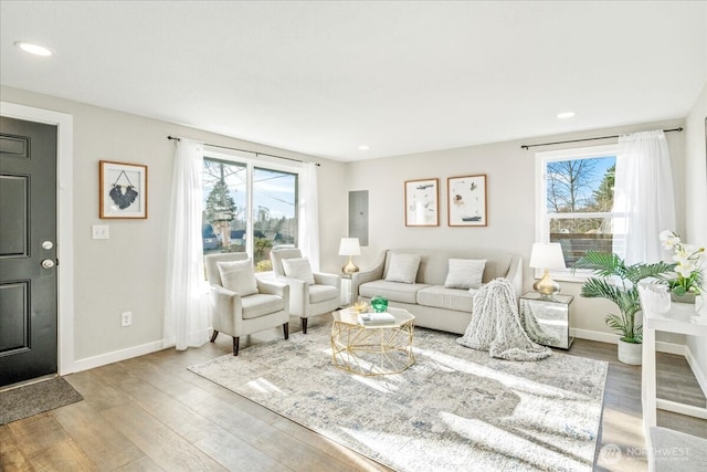 living area with recessed lighting, wood finished floors, electric panel, and baseboards