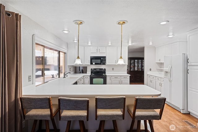 kitchen featuring sink, white cabinetry, hanging light fixtures, a kitchen breakfast bar, and black appliances