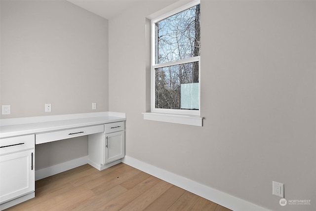 unfurnished office featuring built in desk and light wood-type flooring