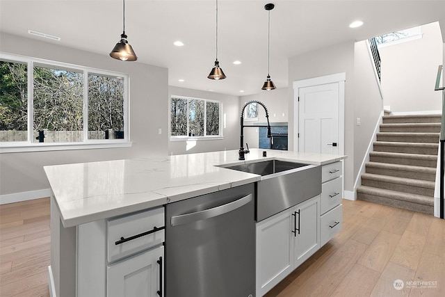 kitchen with dishwasher, light stone countertops, white cabinets, a center island with sink, and decorative light fixtures