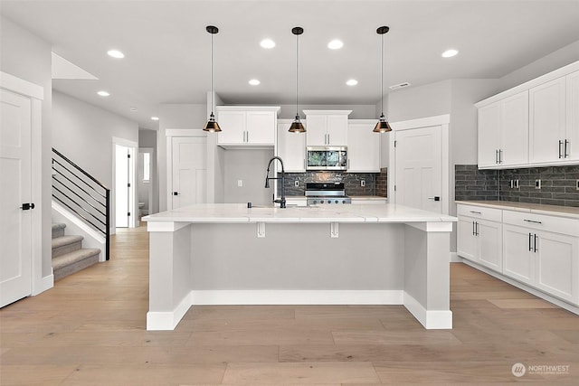 kitchen featuring white cabinetry, range, an island with sink, and hanging light fixtures