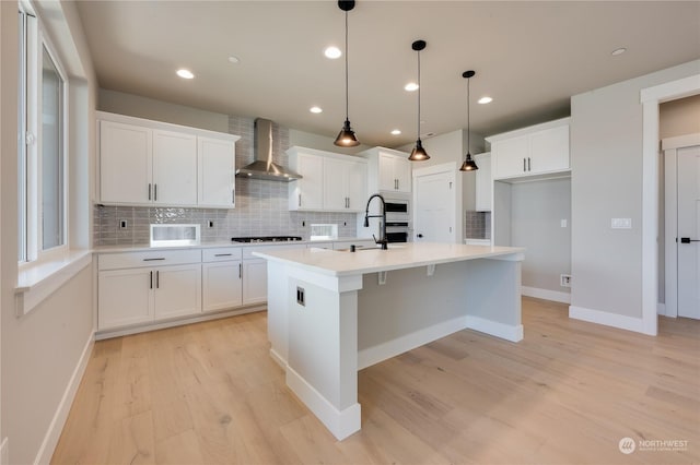 kitchen featuring pendant lighting, white cabinets, a kitchen island with sink, gas cooktop, and wall chimney range hood