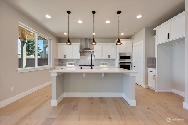 kitchen featuring pendant lighting, white cabinets, stainless steel oven, and wall chimney exhaust hood