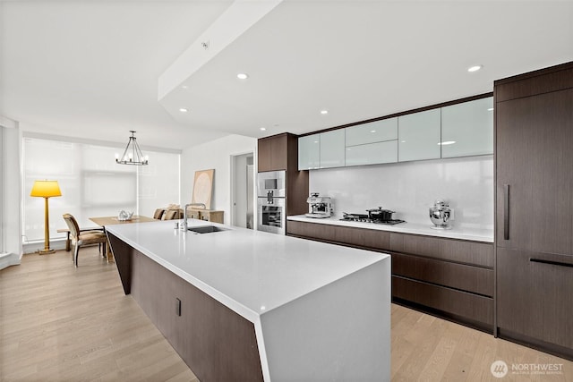 kitchen with sink, white cabinetry, a center island with sink, light wood-type flooring, and stainless steel gas stovetop