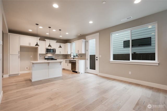 kitchen with a center island, hanging light fixtures, appliances with stainless steel finishes, decorative backsplash, and white cabinets