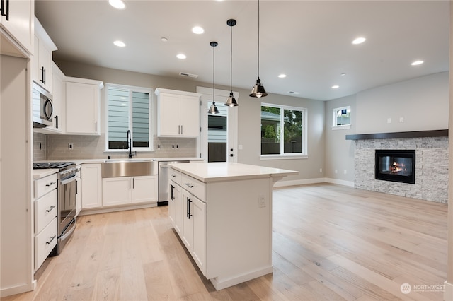 kitchen with sink, white cabinetry, stainless steel appliances, a center island, and decorative light fixtures